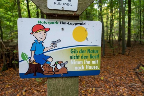 Sign with the inscription Don't give nature the rest! Take it home with you. under hiking signs in the autumnal forest