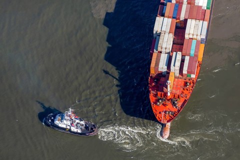 Aerial view of a tugboat pulling a container ship on the Elbe and giving direction
