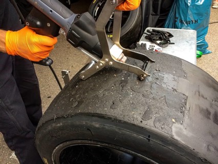 Race mechanic cleans surface of racing tyres slicks makes reconditioning spreads used tyres again for reuse at car races