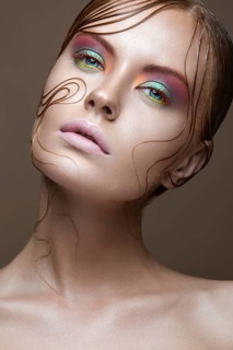 Beautiful girl with bright colored makeup and wet strands of hair on the face. Creative image. Picture taken in the studio