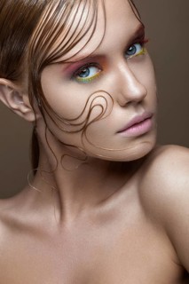 Beautiful girl with bright colored makeup and wet strands of hair on the face. Creative image. Picture taken in the studio