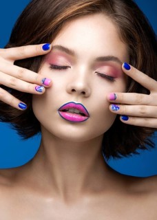 Beautiful model girl with bright makeup and colored nail polish. Beauty face. Short colorful nails. Picture taken in the studio on a blue background