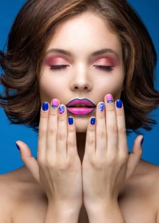 Beautiful model girl with bright makeup and colored nail polish. Beauty face. Short colorful nails. Picture taken in the studio on a blue background