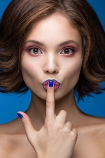 Beautiful model girl with bright makeup and colored nail polish. Beauty face. Short colorful nails. Picture taken in the studio on a blue background