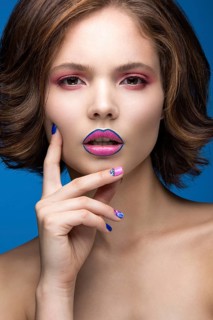 Beautiful model girl with bright makeup and colored nail polish. Beauty face. Short colorful nails. Picture taken in the studio on a blue background