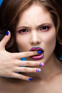 Beautiful model girl with bright makeup and colored nail polish. Beauty face. Short colorful nails. Picture taken in the studio on a blue background