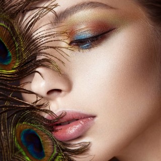 Beautiful girl with bright colored makeup and peacock feather on her face. Beauty face. Close-up. Photos shot in the studio