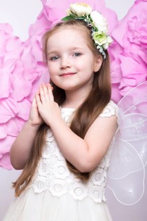 Little fairy girl in white dress on a background of flowers. Photo taken in studio