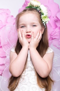 Little fairy girl in white dress on a background of flowers. Photo taken in studio