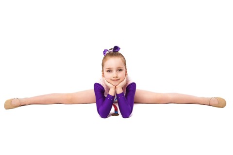 Little girl gymnast with a medal in a sports swimsuit doing exercises. Photo taken in the studio on a white background