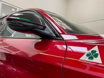 Detail of rear view mirror with carbon optic fairing with coloured stripes of Italian national colour flag Tricolore historical modern signet logo marking of Alfa Romeo Quadrifoglio green four-leaf cl...