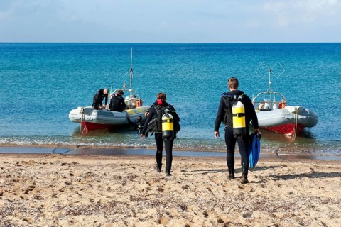 Divers Sport divers running with scuba equipment compressed air tanks across beach sandy beach from Mediterranean Sea to inflatable boat