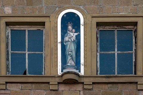 Figure of a saint on a house facade in a niche behind glass