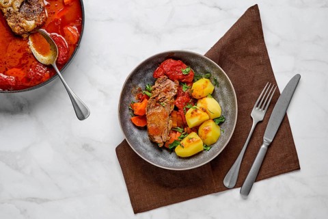 Slow cooking food. Stewed bottom round roast beef meat in beer gravy with tomatoes and carrot