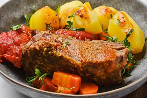 Closeup view of bottom round roast beef meat baked in beer gravy with tomatoes and carrot