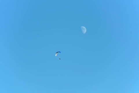 Paramotor in flight on a sunny day with the moon in the sky. France