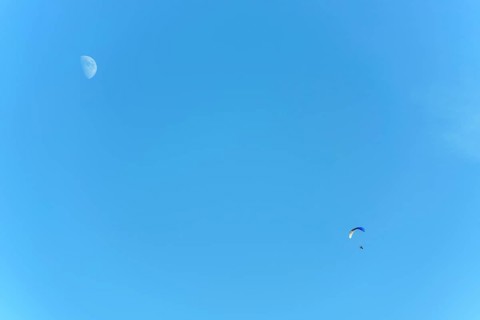 Paramotor in flight on a sunny day with the moon in the sky. France