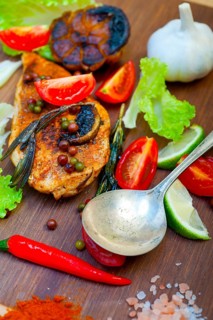 Wood fired hoven cooked chicken breast on wood board with herbs spices and vegetables