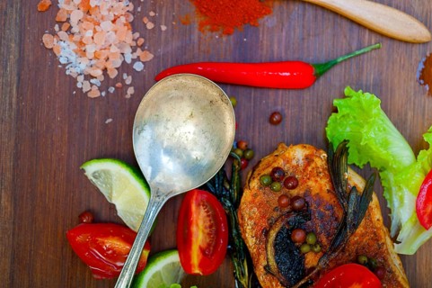 Wood fired hoven cooked chicken breast on wood board with herbs spices and vegetables