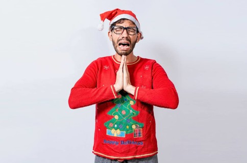 Man with christmas hat with hands together in pleading gesture. Christmas guy with hands together begging for a Christmas wish