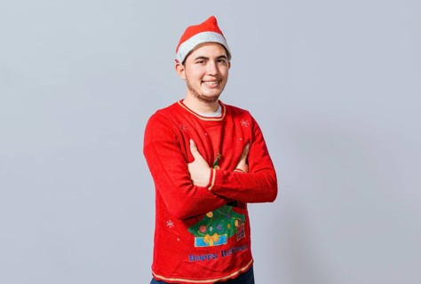 Portrait of guy in sweater and christmas hat with crossed arms isolated. Smiling guy in christmas hat with crossed arms smiling. Teenage guy in christmas clothes with crossed arms smiling