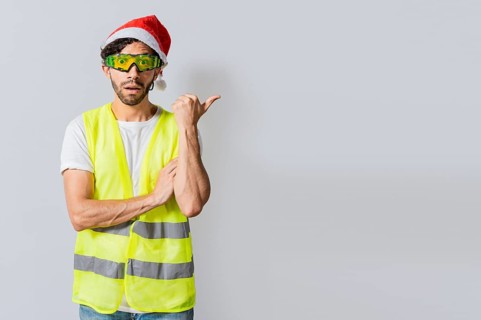 Amazed builder engineer in christmas hat pointing a copy space. Engineer man in christmas hat showing a product