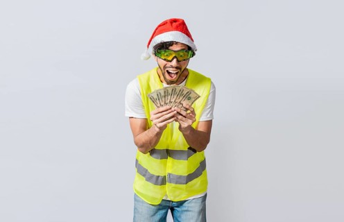 Builder engineer in christmas hat with happy expression holding dollars isolated. Concept of engineer with money in holiday season