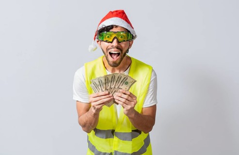Engineer in christmas hat holding money smiling at camera. builder engineer in christmas hat with happy expression holding dollars isolated. Concept of engineer with money in holiday season