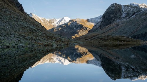 Slightly snow-covered mountains reflected in Schwarzsee in autumn on the Flueela Pass