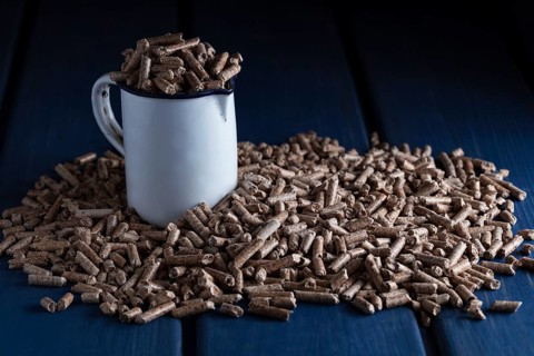 Wood pellets with enamel cup on blue wooden background