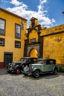 Vintage cars parked in front of yellow gate and wall