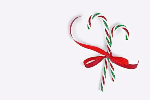 Striped candy canes tied together with red ribbon on side of white background with copy space