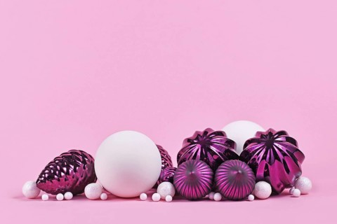 Christmas arrangement with purple and white tree ornament glass baubles on pink background with empty copy space