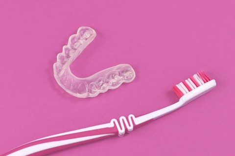 Customized transparent teeth bite guard clear aligners for lower jaw with tooth brush on pink background