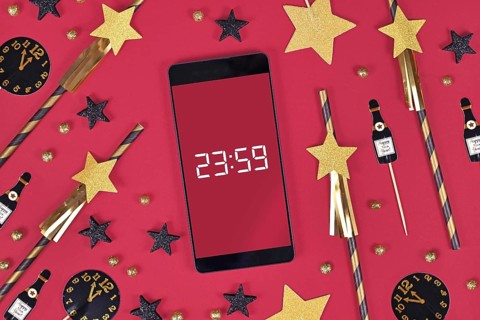New Year Silvester celebration concept with smart phone with timer countdown to midnight between party items like paper straws and paper champaign bottles on dark pink background