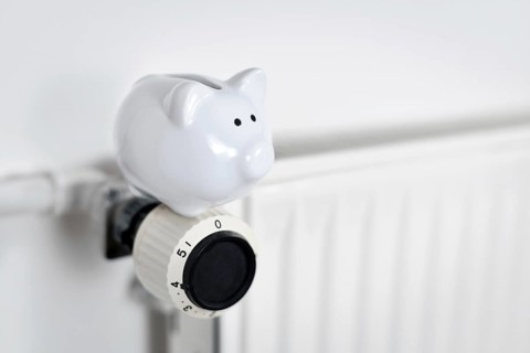 Saving money for gas for heating concept with piggy bank on radiator with copy space