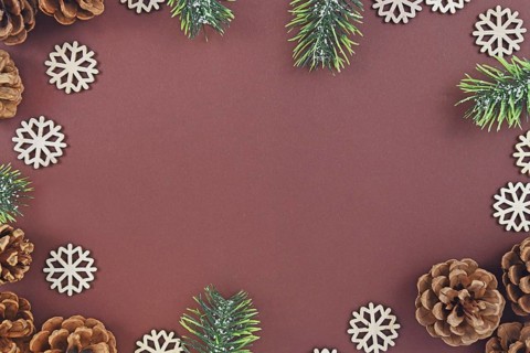 Seasonal Christmas flat lay with pine or fir cones and branches and wooden snowflake ornaments surrounding brown background with empty copy space like a border