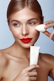 Beautiful girl with red lips and classic makeup with foundation and sponge in hand. Beauty face. Photo taken in the studio