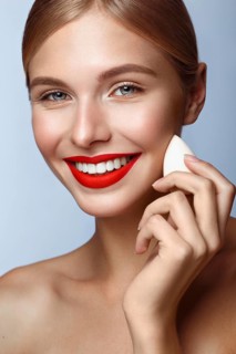 Beautiful girl with red lips and classic makeup with foundation sponge in hand. Beauty face. Photo taken in the studio