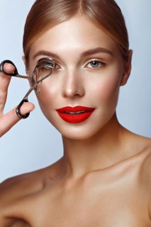 Beautiful girl with red lips and classic makeup with curler in hand. Beauty face. Photo taken in the studio