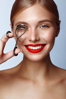 Beautiful girl with red lips and classic makeup with curler in hand. Beauty face. Photo taken in the studio