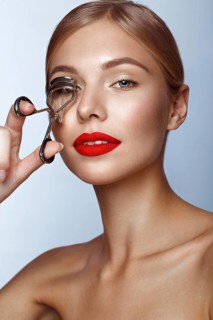 Beautiful girl with red lips and classic makeup with curler in hand. Beauty face. Photo taken in the studio