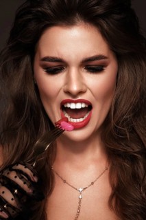 Beautiful girl with red lips and classic makeup and curls with lipstick in hand. Beauty face. Photo taken in the studio
