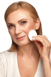 Portrait of a beautiful elderly woman in a white shirt removing makeup with a cleanser and a cotton pad
