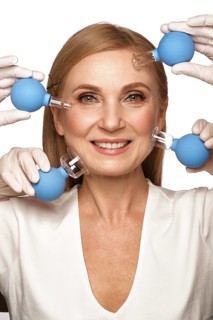 Portrait of a beautiful elderly woman in a white shirt with classic makeup and blond hair with massage tools in her hands