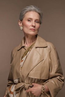 Portrait of a beautiful elderly woman in a beige raincoat with classic makeup and gray hair