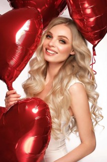 Sexy woman in white dress and balloons with hearts posing in the studio on Valentine's Day