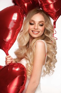 Sexy woman in white dress and balloons with hearts posing in the studio on Valentine's Day