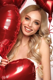 Sexy woman in white dress and balloons with hearts posing in the studio on Valentine's Day