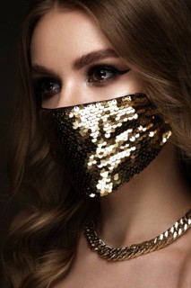 Portrait of a beautiful woman in a gold mask with sequins and classic makeup. Mask mode during the covid pandemic